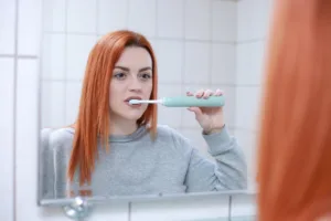 Femme se brossant les dents avec une brosse à dents électrique devant un miroir